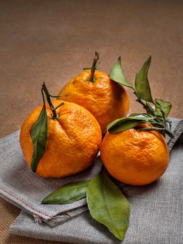Fresh, tasty, sweet, large with branches and green leaves orange mandarins for healthy and dietary food stand a bunch on a large liana napkin
