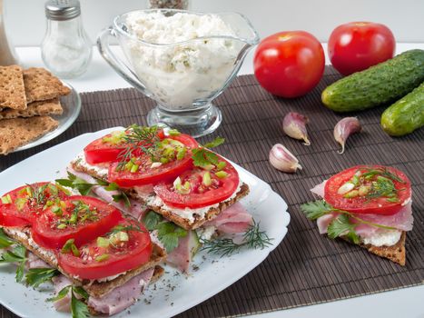 Sandwiches with rustling bread from buckwheat flour smeared with curd cheese on top is ham, tomato with greens and spices is shown close up