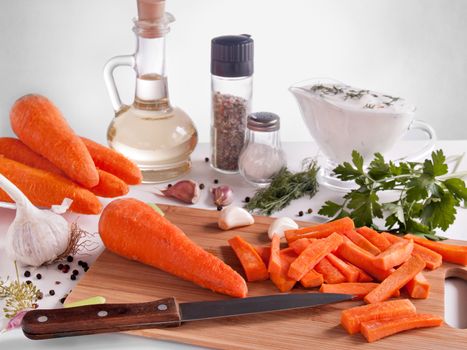 Carrots chopped on chopsticks surrounded by greenery, parsley, dill, garlic, pepper, vegetable oil in a bottle with a stopper, pepper and salt in jars, cream with greens in a glass, vegetable cutting knife, diet and healthy food, new Harvest of vegetables
