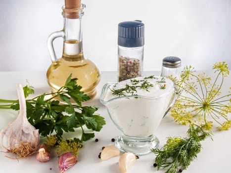 Cooked sour cream sauce with garlic, herbs, parsley, dill, herbs, pepper in a glass bowl on a white background with butter in a bottle, with pepper and salt jars