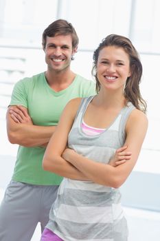 Portrait of a fit young couple standing with arms crossed in bright exercise room