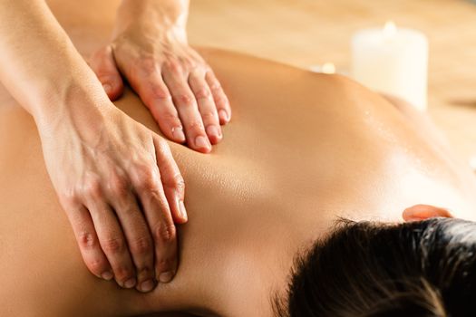 Close up macro detail of hands massaging female upper back and shoulder in spa. Ambient candlelight in background.