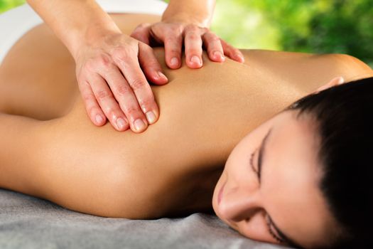 Close up of hands massaging female back and shoulder against green background.