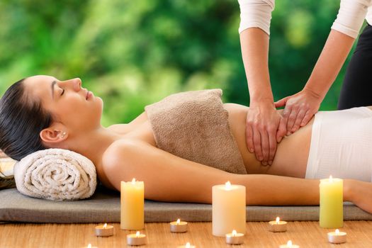 Close up portrait of woman enjoying curative Ayurvedic massage against green nature background. Therapist massaging belly.