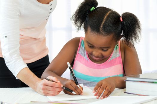 Close up of little african girl doing school work with caucasian teacher supervising.