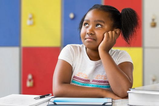 Close up portrait of little african female student sitting at desk in classroom. Tedious kid with bored wondering facial expression staring and looking up.
