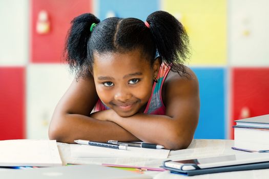 Close up portrait of little african student resting with head on arms in classroom.Girl showing bored facial expression.