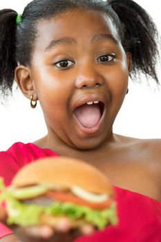 Close up face shot of expressive little african girl with open mouth and big eyes about to eat hamburger.Kid holding meat hamburger infant of face isolated on white background.
