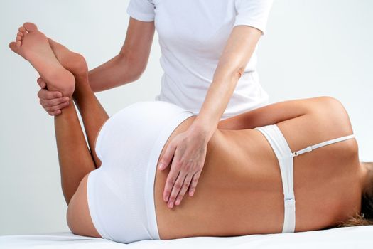 Therapist doing lower back massage on woman.Osteopath rotating woman’s legs.