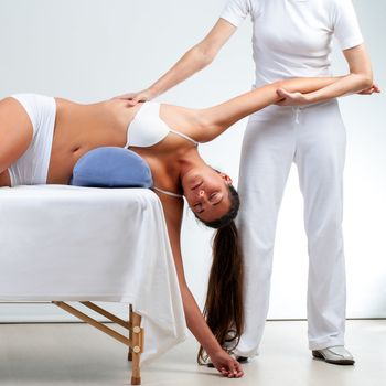 Osteopath stretching woman’s shoulder on massage bed at session.