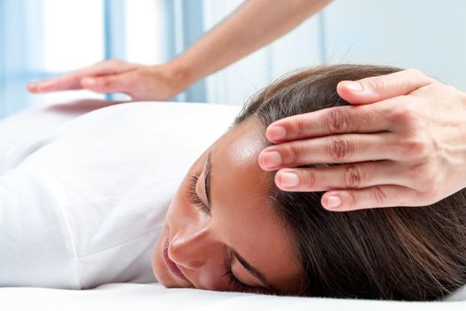 Therapists hands doing reiki therapy on girl. One hand on head and one hand on back.