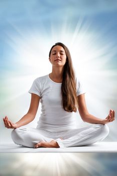 Close up portrait of attractive young woman meditating with eyes closed. Front view of woman dressed in white in yoga position with ray of light in background.