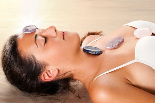 Close up of attractive young woman meditating with eyes closed. Precious gemstones on top of forehead and chest.