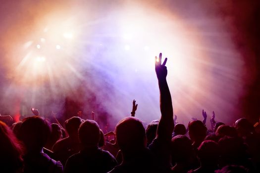 Dancing Crowd of young people dancing at disco. People Raising hands against purple and pink smoky background with light beams.