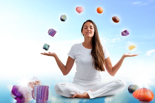 Full length portrait of young woman dressed in white doing yoga with precious gemstones.Conceptual dream scape with colorful gemstones floating around girl.