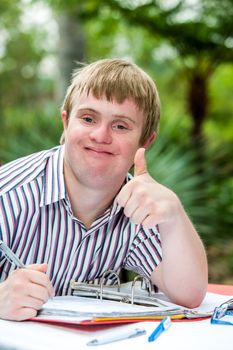 Close up portrait of handicapped student doing thumbs up at desk outdoors.