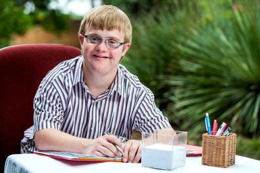 Close up portrait of handicapped student wearing glasses at desk in garden.