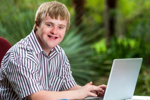 Portrait of happy handicapped young man typing on laptop in garden.