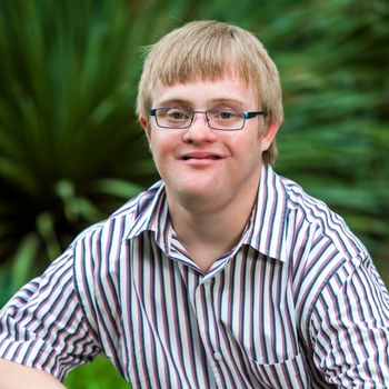 Close up portrait of handicapped boy in garden wearing glasses.