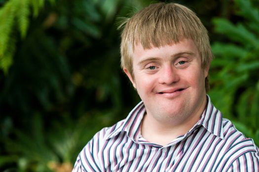 Close up portrait of young handicapped man with green leaves in background.