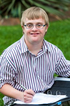 Close up portrait of young handicapped student writing in file outdoors.