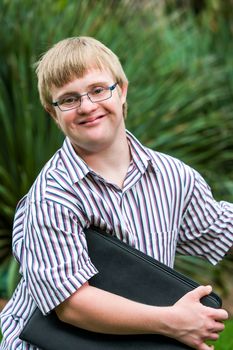 Close up portrait of young student with down syndrome holding files outdoors.