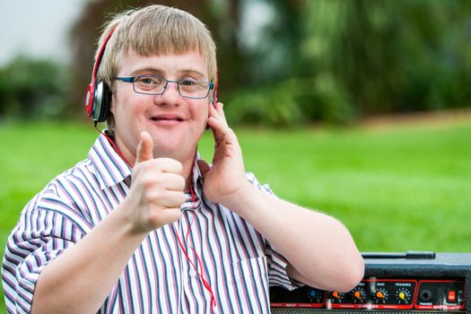 Close up portrait of down syndrome boy with headset doing thumbs up outdoors.