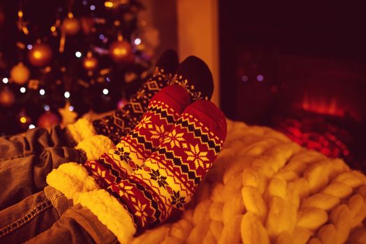 Couple sitting in woolen socks near fireplace in living room decorated for Christmas holidays