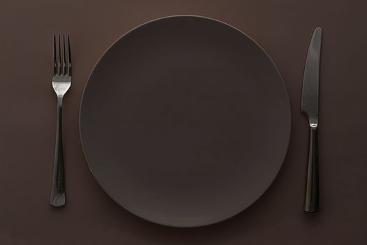 Empty plate and cutlery as mockup set on dark brown background, top tableware for chef table decor and menu branding design