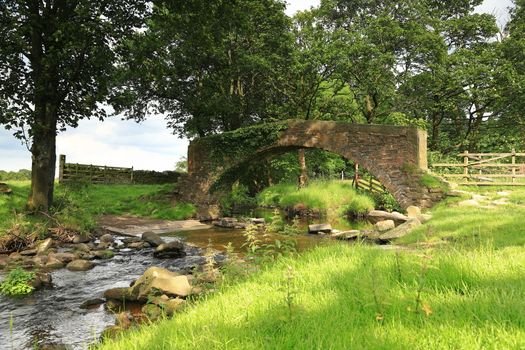 A stone bridge crosses a stream in the West Yorkshire countryside close to the village of Haworth in northern England.