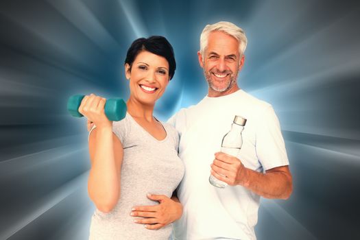 Happy fit couple with dumbbell and water bottle against abstract background