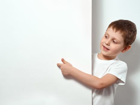 Four-year-old boy shows finger on blank white sheet. Happy child in white t-shirt over white background with copy space for message, mock up