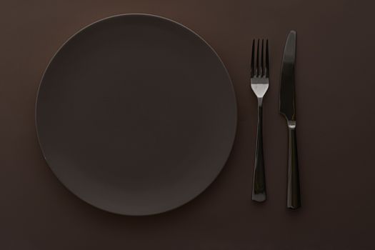 Empty plate and cutlery as mockup set on dark brown background, top tableware for chef table decor and menu branding design
