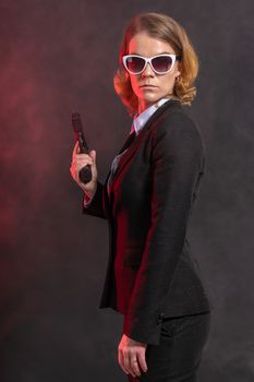 mafian woman with a gun in her hand. portrait on a dark background with red light. white glasses