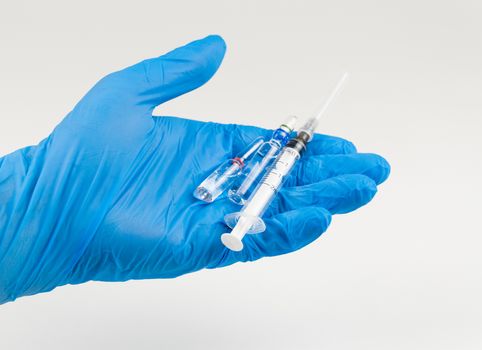 Hand in glove holds a syringe and a vaccine on a white background. Coronavirus Protection Concept