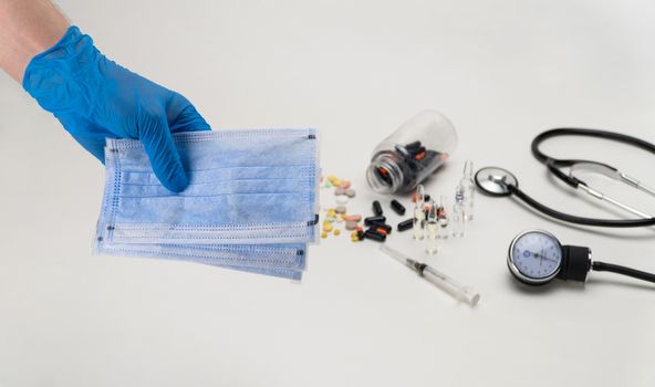 Hand holding a medical mask against the background of a stethoscope and tonometer. Coronavirus Protection Concept