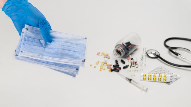 Hand holding a medical mask against the background of a stethoscope and pills. Coronavirus Protection Concept