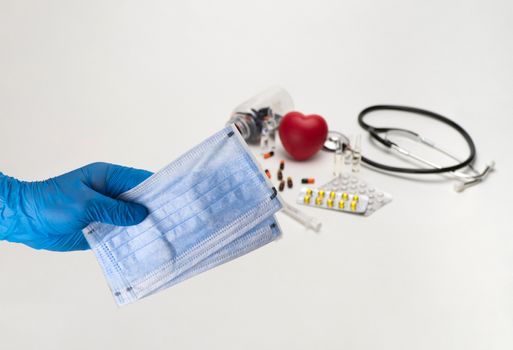 Hand holding a medical mask against the background of a stethoscope and tablets. Coronavirus Protection Concept