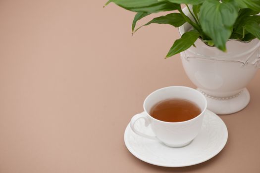cup of tea on a saucer and a flower on a light brown background