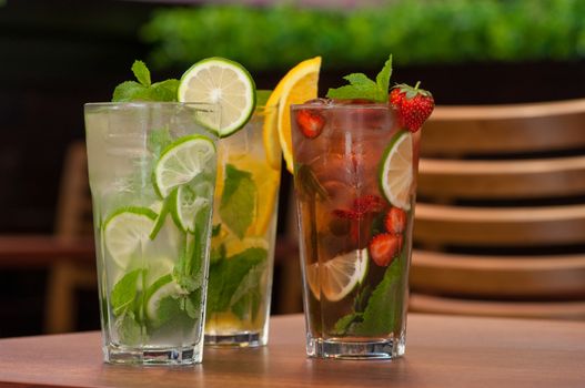 three cold drinks with citrus and strawberries in a glass on the table