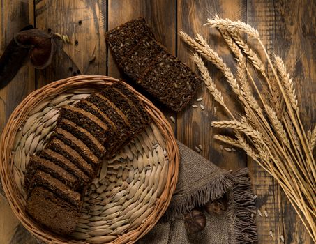 Sliced bread in a wicker tray and spikelets on wooden surface
