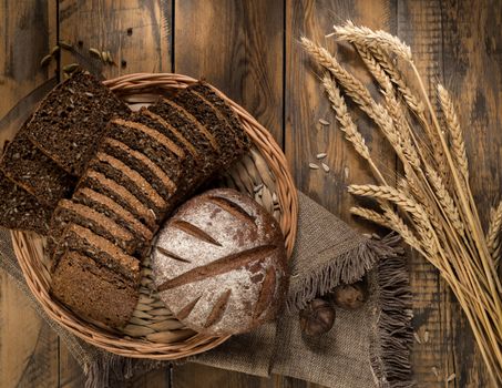 Round and sliced bread in a wicker tray with spikelets wooden surface with cloth