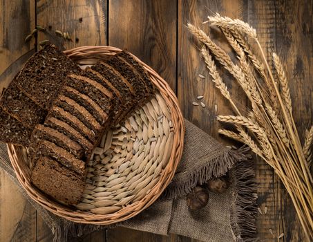 Sliced rye bread in a wicker tray and spikelets on wooden surface