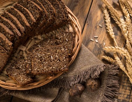 bread in a wicker tray with a napkin and spikelets on wooden surface, view from above