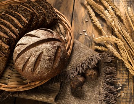 Round and sliced bread in a wicker tray with spikelets wooden surface with cloth