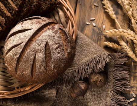 round rye bread in a wicker tray with a napkin and spikelets on wooden surface