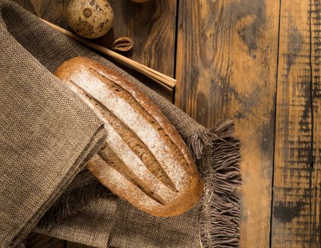 a loaf of bread on a cloth napkin on a wooden surface, top view