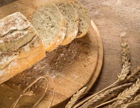 closeup of sliced bread on a round wooden tray with spikelets and crumbs