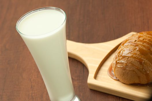 bread drizzled with honey on a wooden plate and a glass of milk