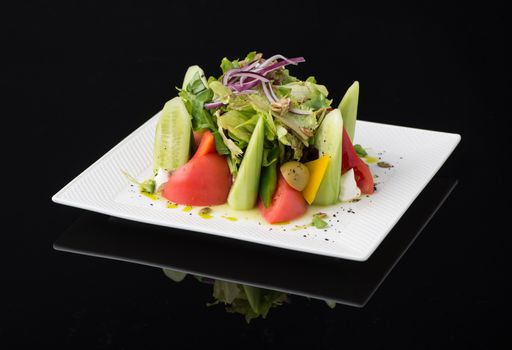 vegetable salad in a square plate on a black background, isolated